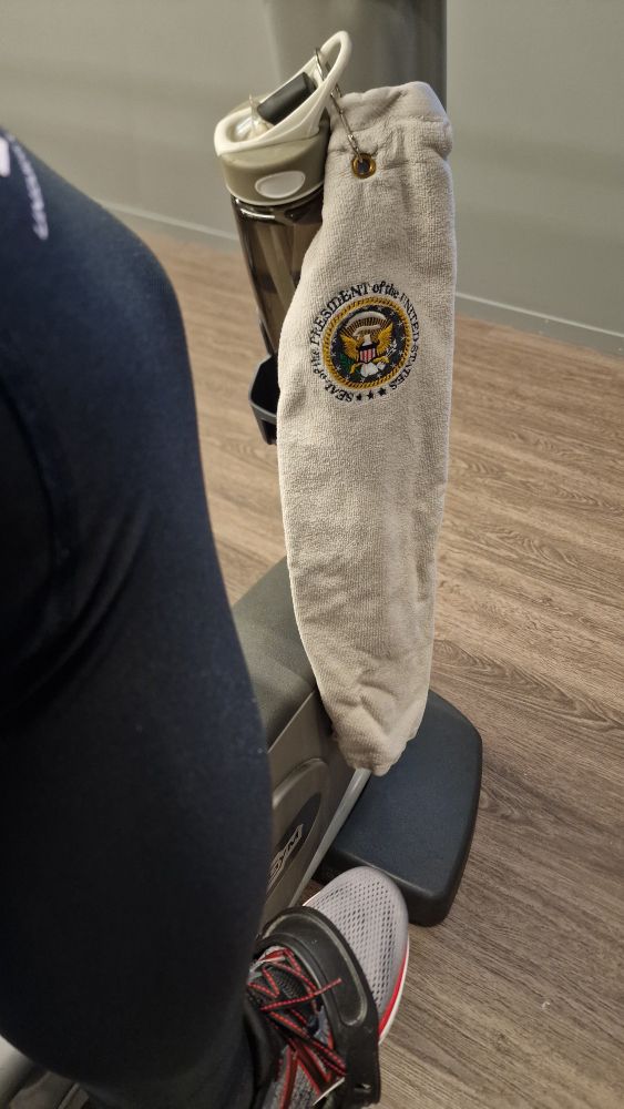 Treningshåndkle med det amerikanske presidentemblemet brodert inn, hengende fra en vannflaske på en ergometersykkel 