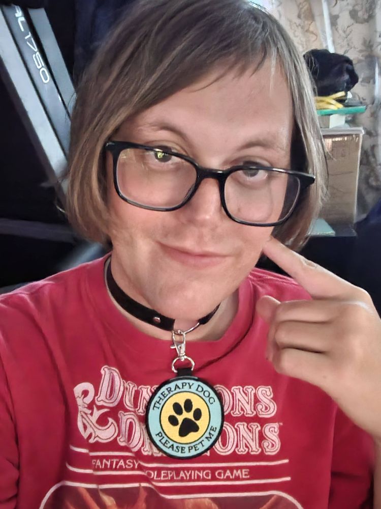 aisha smiling and wearing a heart choker with a big tag attached that says "Therapy Dog | Please Pet Me"