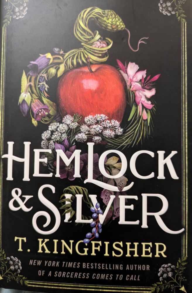 The dust jacket of a book showing a red apple encircled by a snake & bundles of herbs with the title Hemlock & Silver and the author name T Kingfisher .