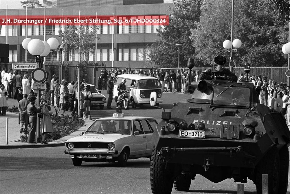 Straßenszene mit dem Bundeskanzleramt im Hintergrund, mehrere Polizeiautos und ein Panzerfahrzeug im Vordergrund