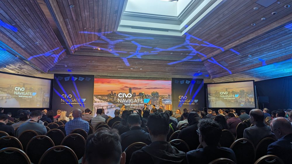 A conference event room with three people on stage, talking