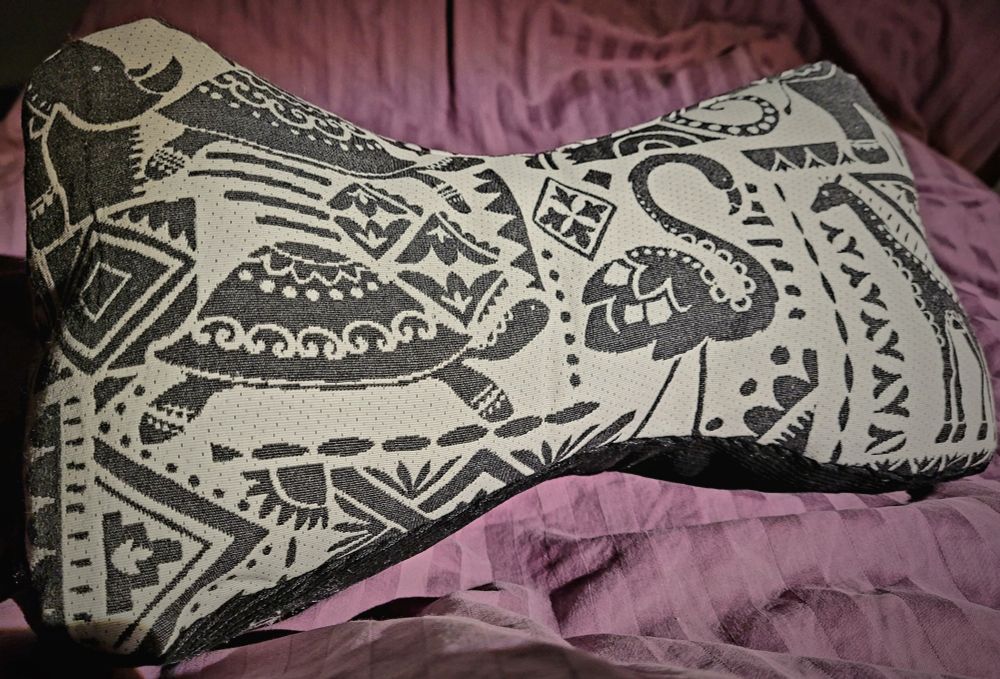 Leseknochen / Nackenkissen aus weißem Stoff mit in Anthrazit gemusterten Tiermotiven und schwarzem Cord.