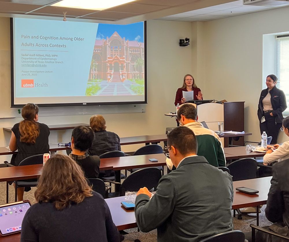 Dr. Morrow introduces Dr. Milani in a hybrid presentation setting with several in-person participants. The screen reads, "Pain and Cognition Among Older Adults Across Contexts," with the UTMB Health logo and a photo of Old Red building.
