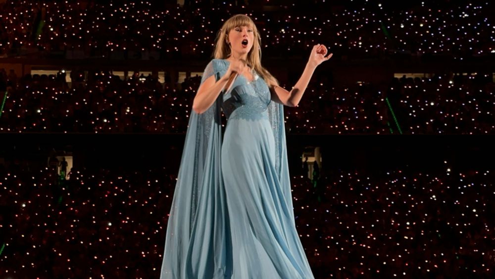 "Taylor Swift singing on stage at the Eras Tour, wearing a sparkly outfit and surrounded by cheering fans during the Folklmore era." 