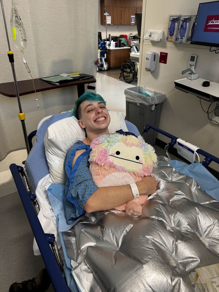 Vin in a hospital bed, holding a rainbow stuffed animal