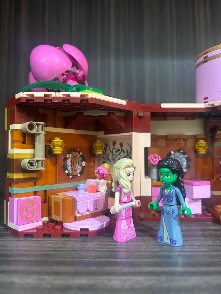 the inside of a lego doll house based on the wicked movie. this picture shows glinda’s side of the dorm room and shows the glinda mini doll in a pink dress and the elphaba mini doll wearing a blue dress
