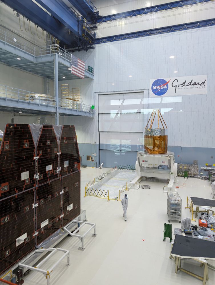 The Roman space telescopes primary mirror apparatus and solar panels are sitting on the floor in a giant clean room at NASA Goddard.