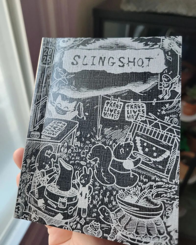 The front cover of the organizer. It says Slingshot and has animals working on a silk screen press with the title Trans Lives Matter.