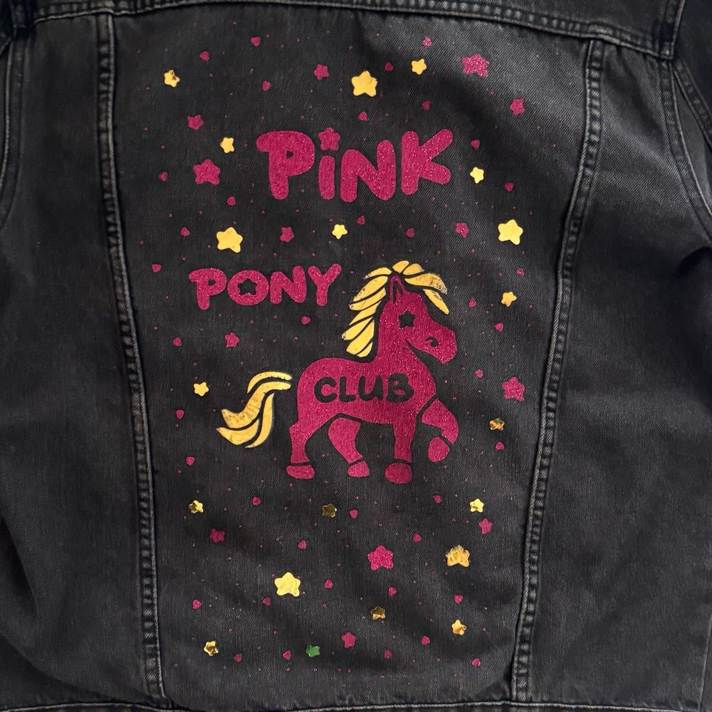 A black denim jacket with a custom art of a Pony, reading Pink Pony Club. The palette is pink and gold, with an array of stars around the Pony. 