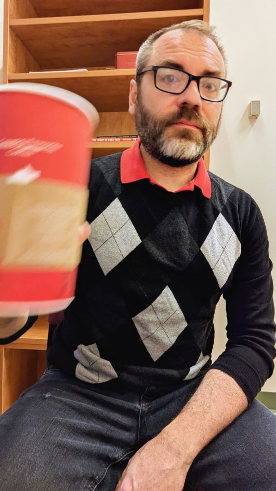 I'm flinging my coffee around in my office wearing a black sweater with grey diamonds on it and a red collar 