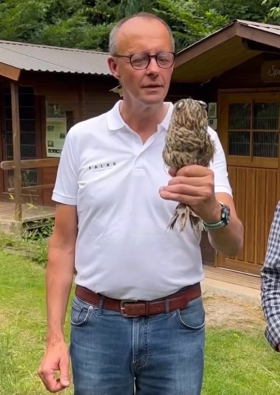 Friedrich Merz hält eine kleine Baby Eule in der Hand, gleich wird er sie fressen, mit Federn und allem. 