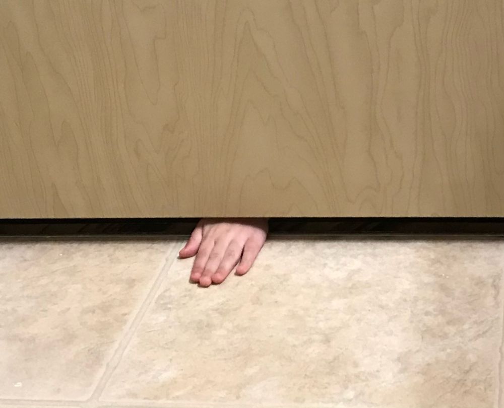 Childs hand sneaking underneath the bathroom door trying to find her mama who just needed one second alone to pee