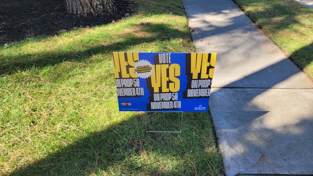 A yard sign on a lawn saying "VOTE YES ON PROP 50 NOVEMBER 4TH", with "ENSURE FAIR REPRESENTATION IN CONGRESS" in a pointy speech bubble