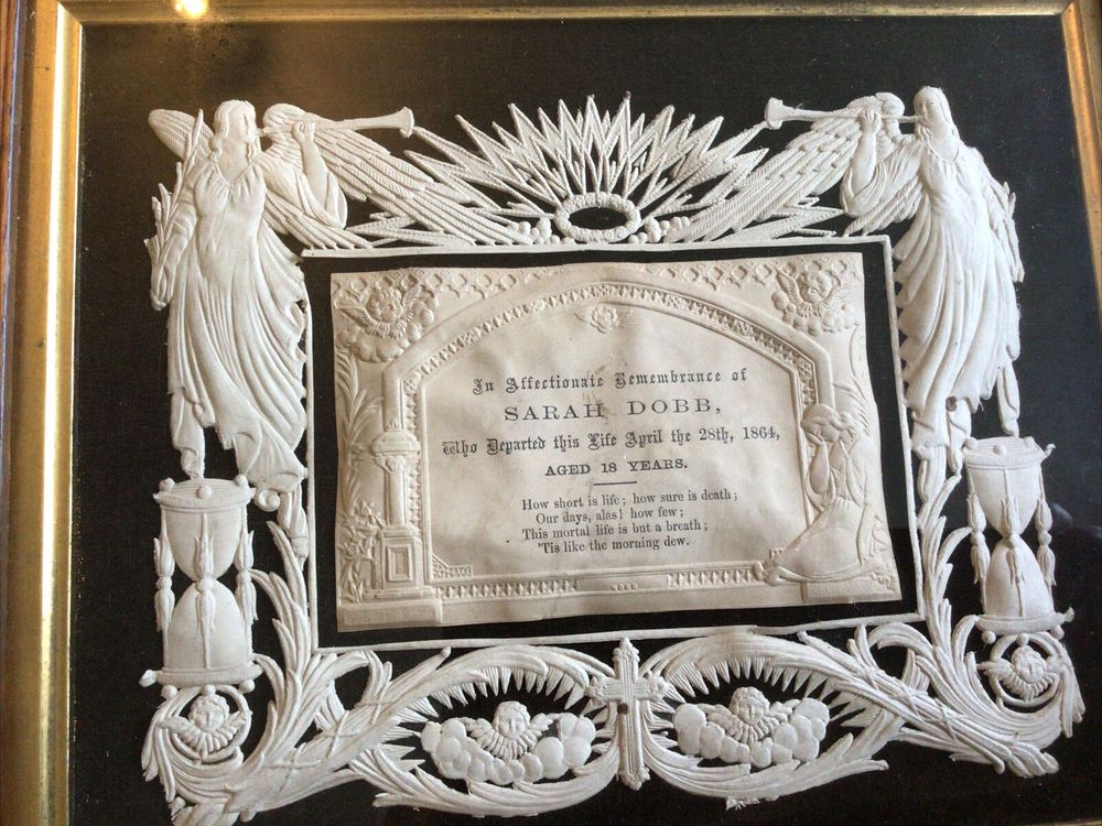 trumpeting angels, cherubs in clouds, hourglasses and a sunburst pressed out of ivory paper, framing a memorial card.