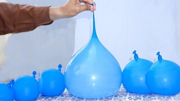 A collection of water balloons with the largest one in the middle being held by someone's hand. 