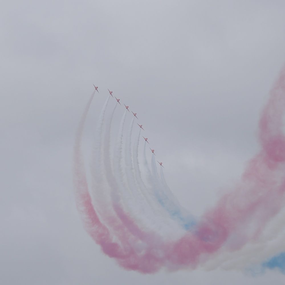 The Red Arrows perform a swooping turn, trailing red, white & blue smoke