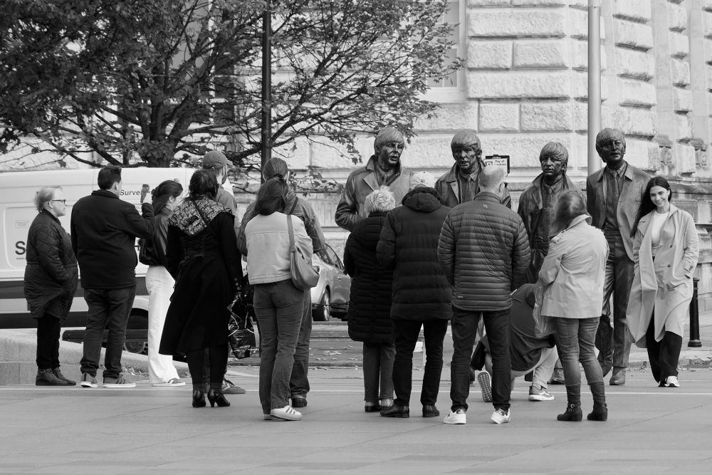 Slightly larger-than-life statues of The Beatles near the Pier Head in Liverpool with a small crowd of people taking photographs.