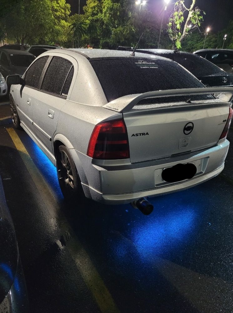 um carro chevrolet astra prata com luzes de neon azul na parte inferior, daora demais