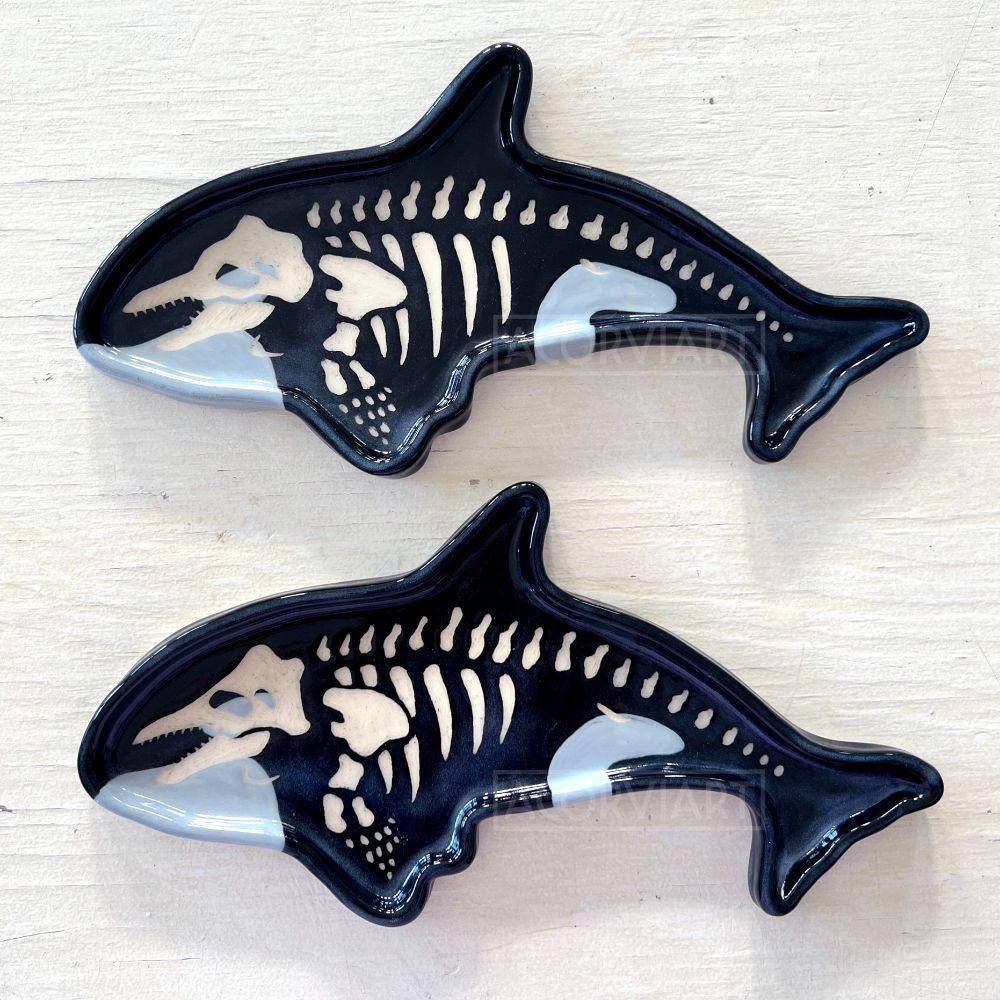 two ceramic plates built and glazed in the shape of orcas, with skeletons sgraffito carved into the surface of the places