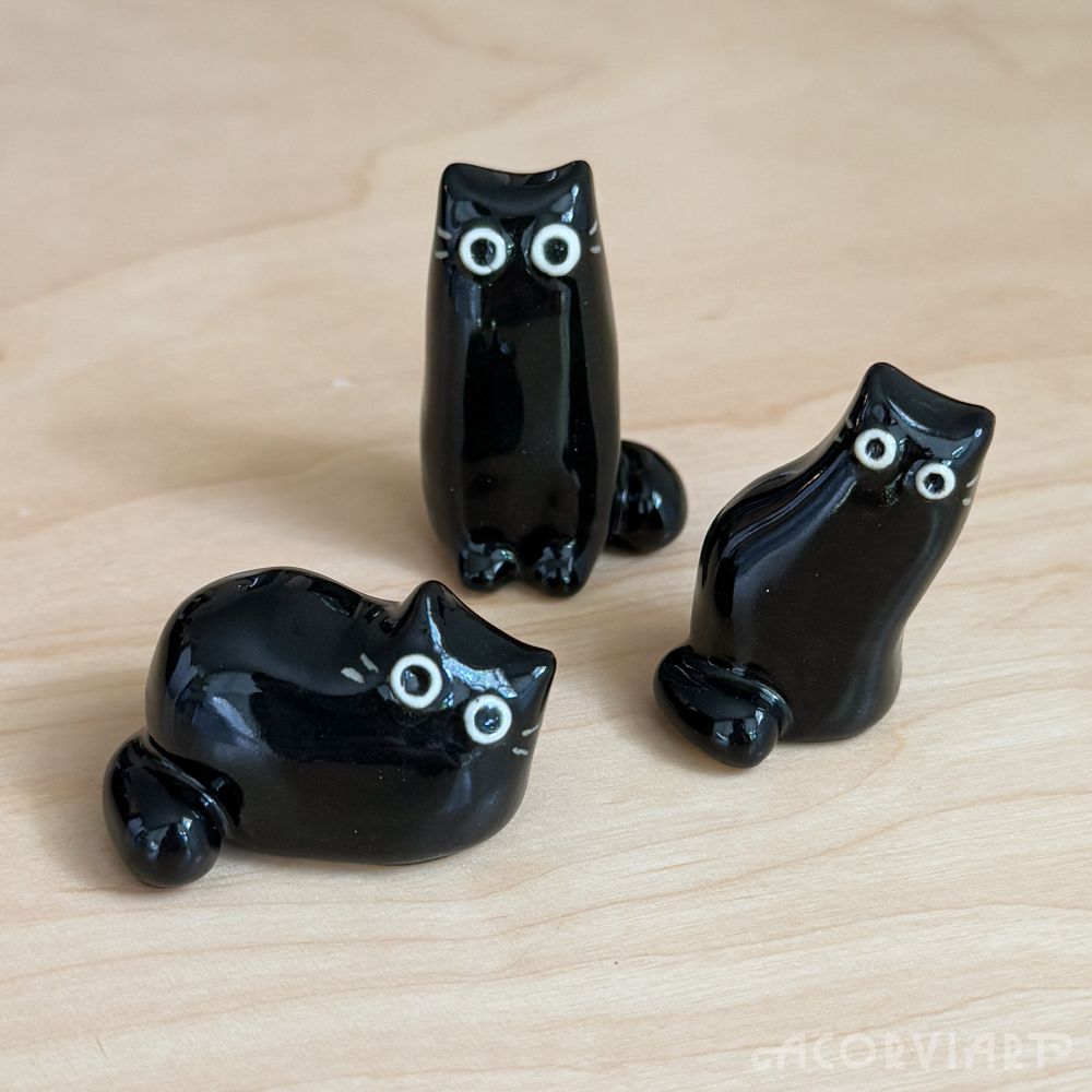 Three black cat ceramic figures—one loafing, one tall, one leaning to the side.