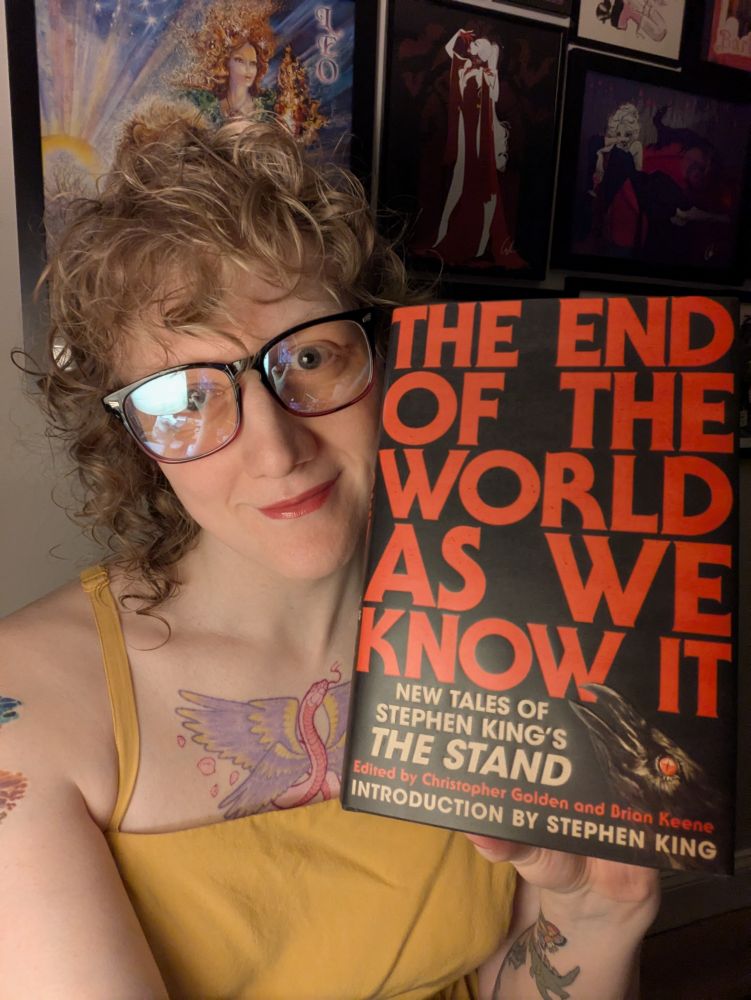 Hailey Piper holding a copy of The End of the World As We Know It: New Tales of Stephen King's The Stand, edited by Christopher Golden and Brian Keene with an Introduction by Stephen King 