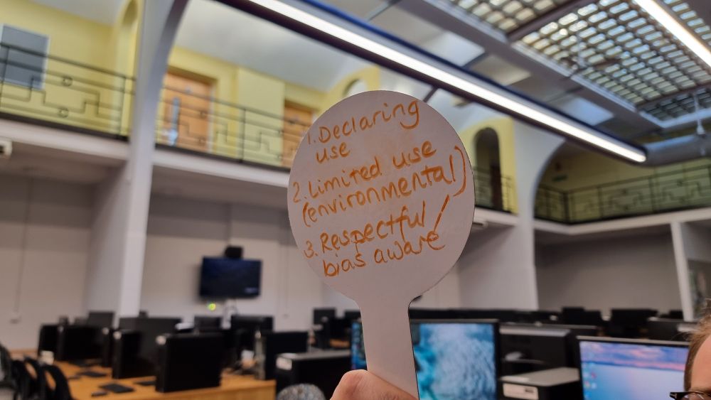 A workshop participants hand holding a mini whiteboard paddle with results of small group discussion. The group's top 3 themes around responsible use of GenAI are "Declaring use, Limited use (environmental), and Respectful/Bias aware".