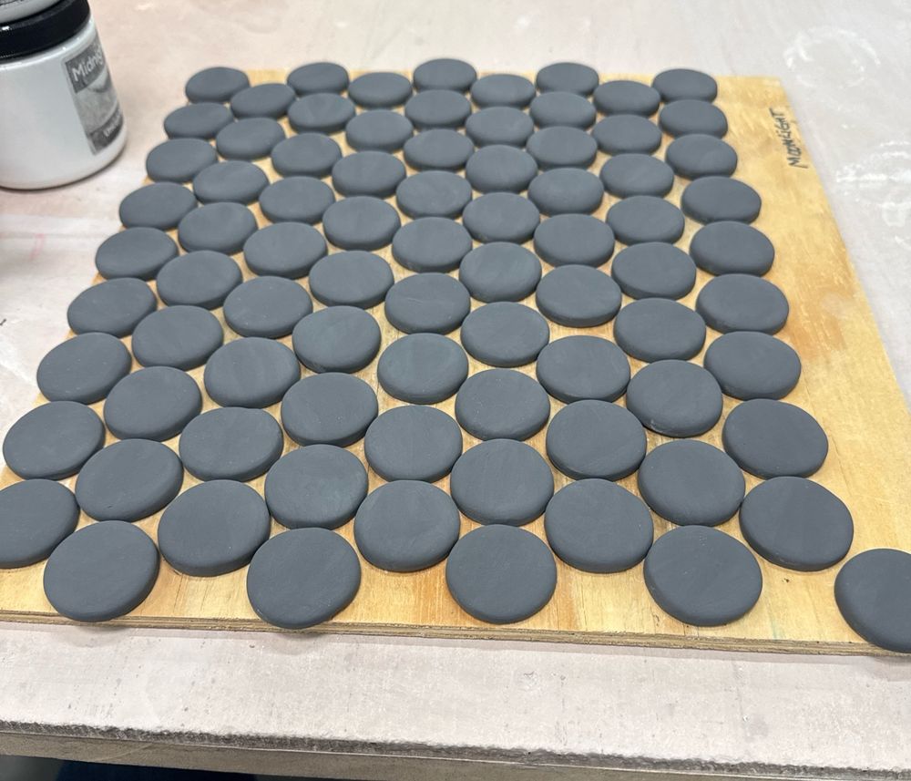Small black ceramic discs sitting in rows on a wooden ware board