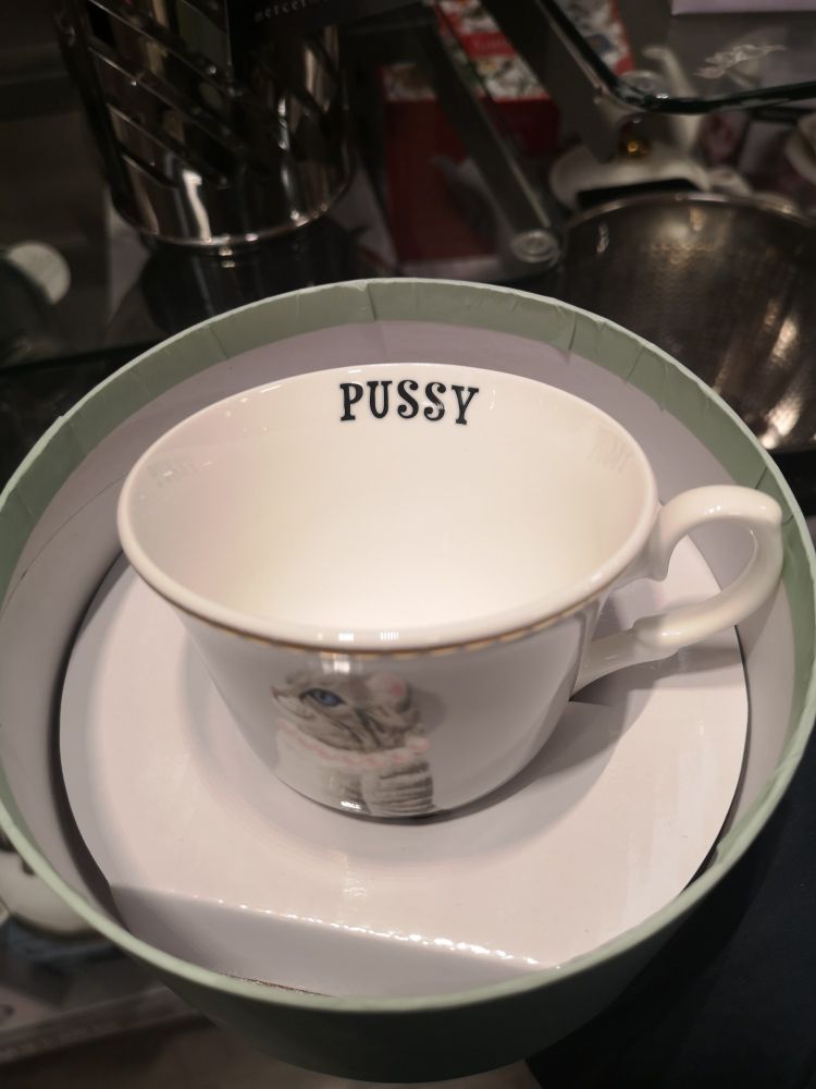 Teacup with a grey cat on the outside and the word "pussy" on the inside rim