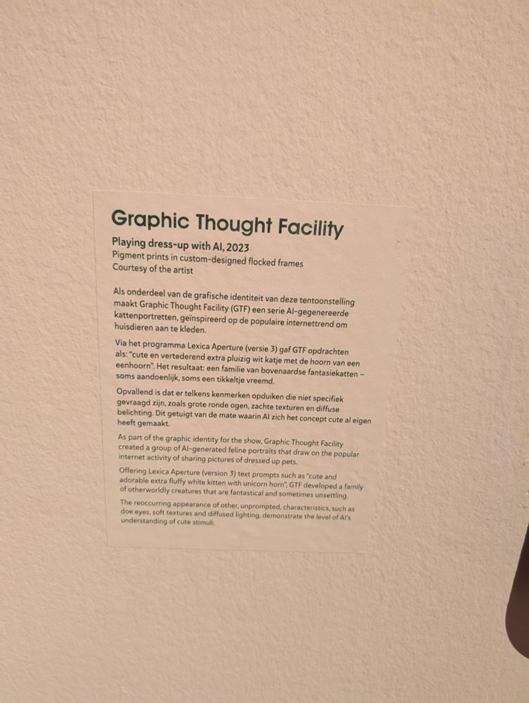 Museum caption with the following text in Dutch, then English

Graphic Thought Facility
Playing dress-up with Al, 2023
Pigment prints in custom-designed flocked frames
Courtesy of the artist
Als onderdeel van de grafische identiteit van deze tentoonstelling
maakt Graphic Thought Facility (GTF) een serie Al-gegenereerde
kattenportretten, geinspireerd op de populaire internettrend om
huisdieren aan te kleden,
Via het programma Lexica Aperture (versie 3) gaf GTF opdrachten
als: “cute en vertederend extra pluizig wit katje met de hoorn van een
eenhoorn”. Het resultaat: een familie van bovenaardse fantasiekatten -
soms aandoenlijk, soms een tikkeltje vreemd.
Opvallend is dat er telkens kenmerken opduiken die niet specifiek
gevraagd zijn, zoals grote ronde ogen, zachte texturen en diffuse
belichting. Dit getuigt van de mate waarin Al zich het concept cute al eigen
heeft gemaakt.
As part of the graphic identity for the show, Graphic Thought Facility
created a group of Al-generated feline portraits that draw on the popular
internet activity of sharing pictures of dressed up pets.
Offering Lexica Aperture (version 3) text Prompts such as “cute and
adorable extra fluffy white kitten with unicorn horn”, GTF developed a family
of otherworldly creatures that are fantastical and sometimes unsettling.
The reoccurring appearance of other, unprompted, characteristics, such as
doe eyes, soft textures and diffused lighting, demonstrate the level of Al's
understanding of cute stimuli.