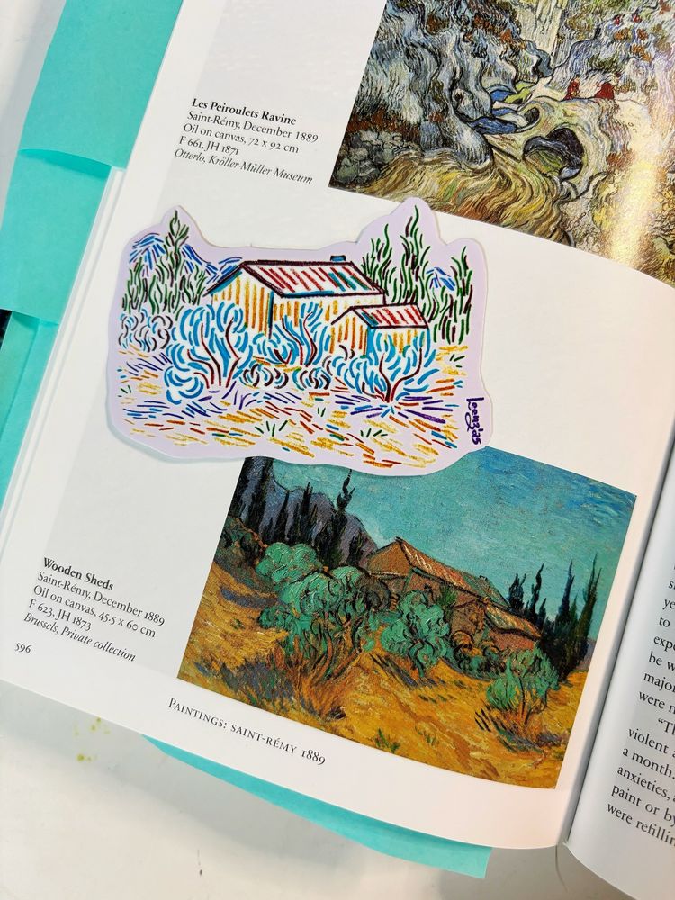 A photo of a 3 inch wide sticker of wooden sheds and cypress trees. The sticker is themed after Vincent Van Gogh’s painting “Wooden Sheds”. The sticker is placed on an open art book next to a picture of the reference painting.
