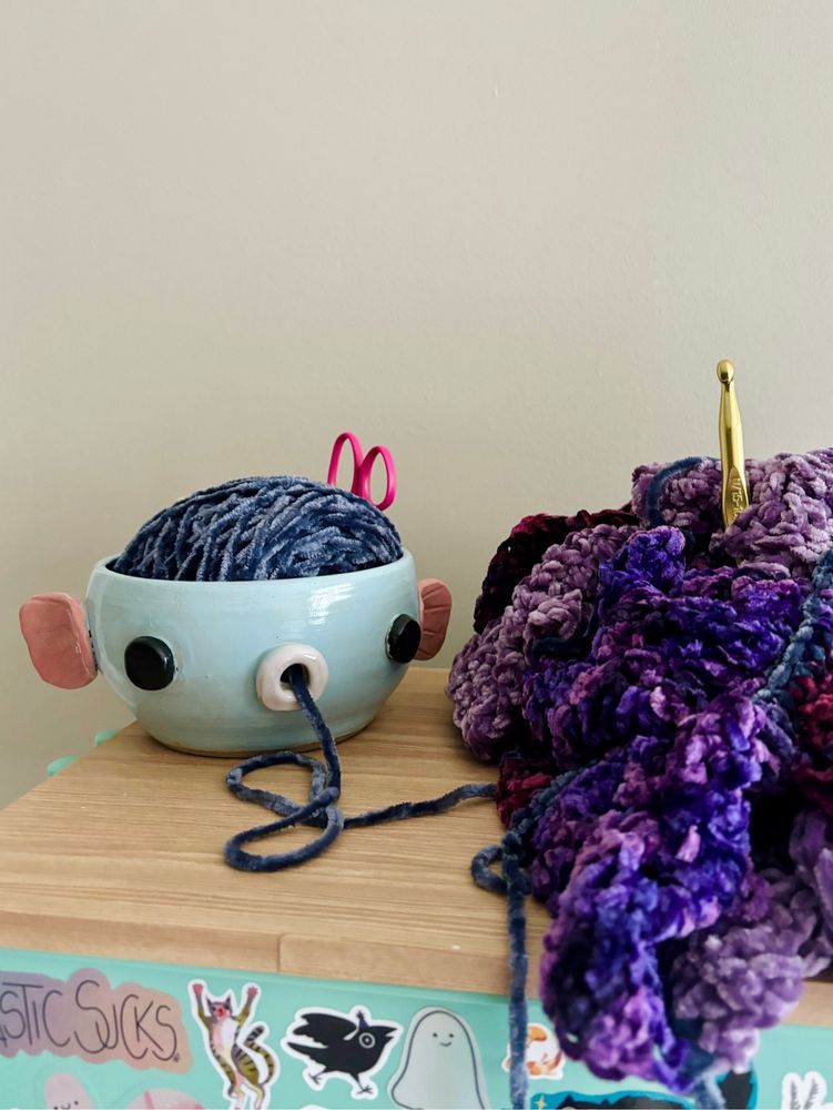 A ceramic bowl that looks like a fish. It has a yarn cake in it and a mouth hole in the side for yarn to go through.