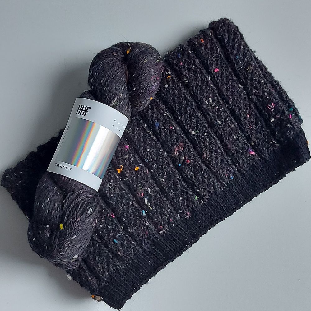 a part of a knitted sweater in black with speckles of colors all over it