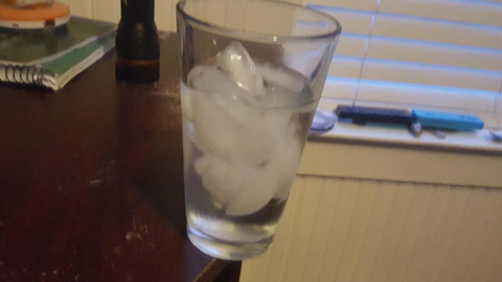 A cup of water very dangerously close to going over a table edge