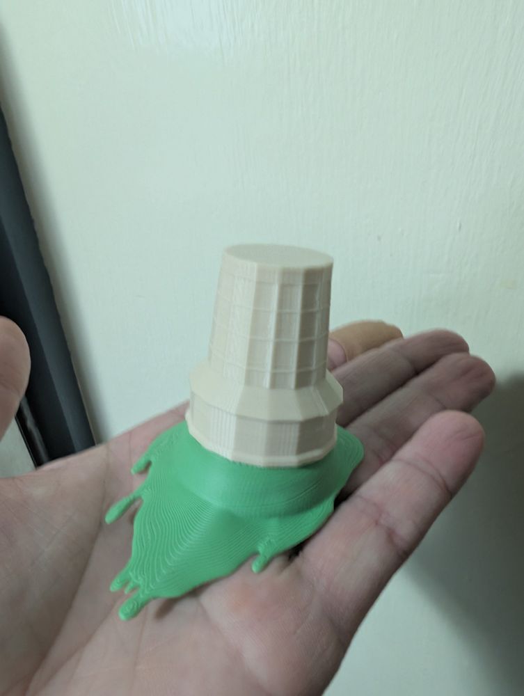 Same 3D printed tan ice cream cone from previous photos printed smaller with green melting ice cream blob attached being held in a hand flat out palm up.