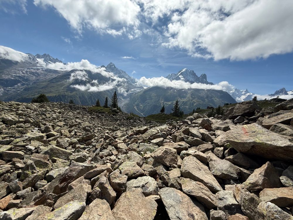 A challenging and rocky path in the Aguilles Rouges region with boulders filling the foreground and majestic mountains and pale blue sky in the distance. 