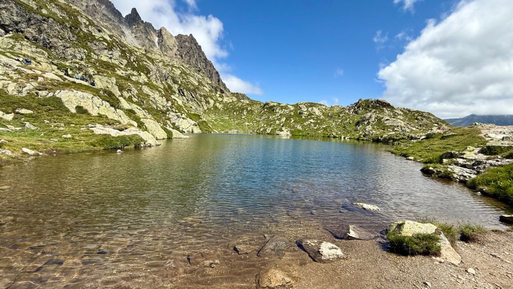 A small clear lake ringed by mountains with blue sky beyond. 