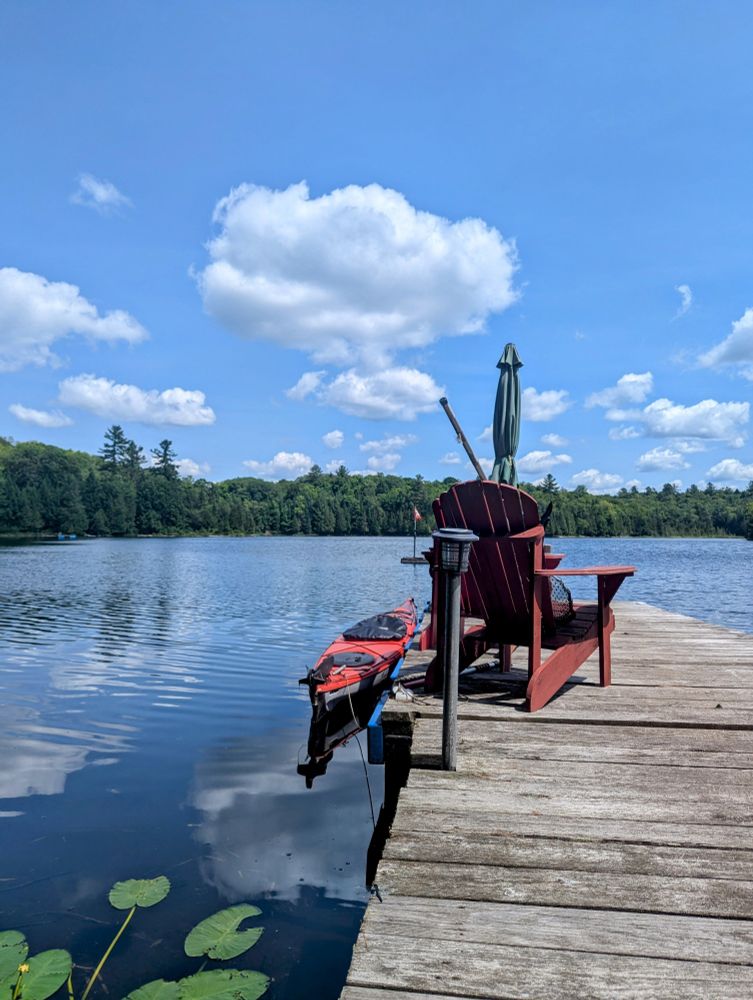 A dock with a few Muskoka (Adirondack) chairs and a kayak on a small quiet lake in the Algonquin Highlands of The Great White North! 🇨🇦
