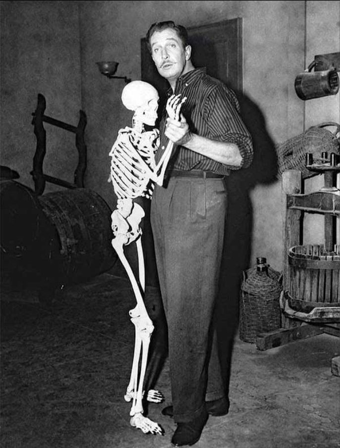 Vincent Price, a tall, well-groomed man dressed in trousers and a short, 'dances' with a skeleton in a basement set