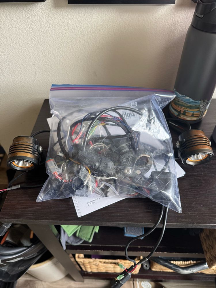 large gallon sized Ziploc bag, full of a snakes nest of miscellaneous wires and electrical components as well as a bracket with two orange auxiliary lights