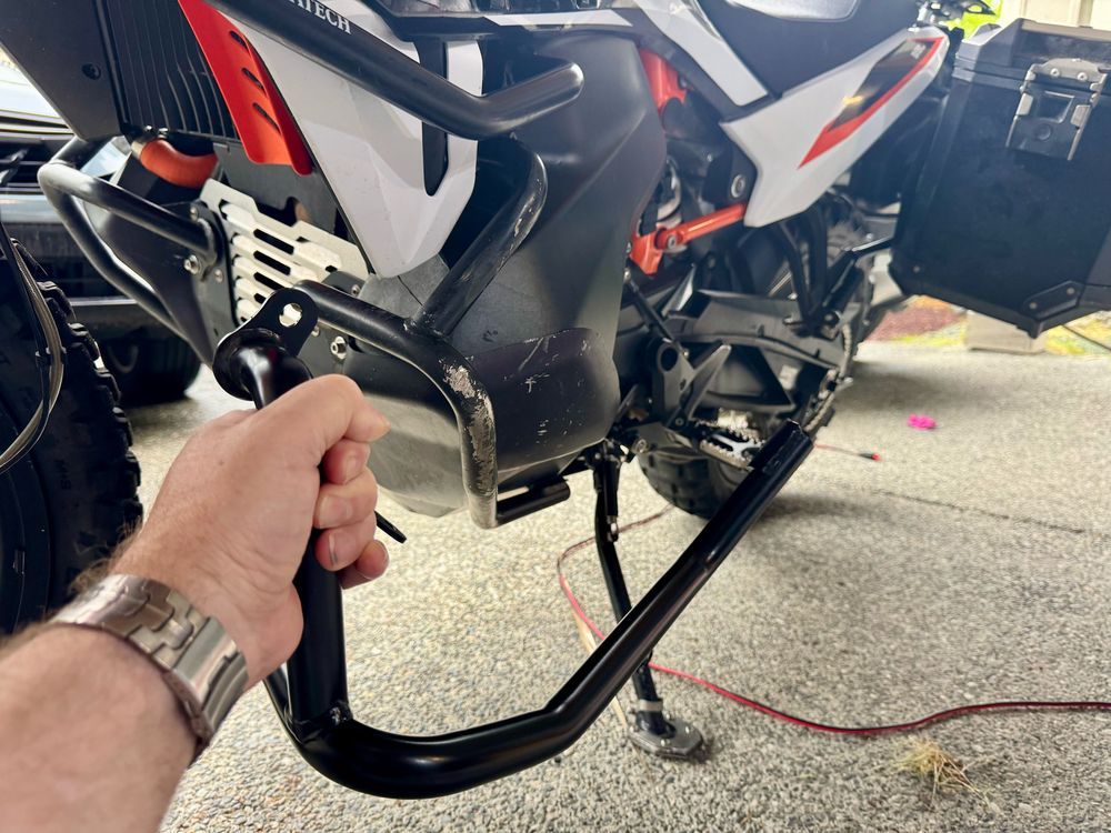 Picture of a Adventure motorcycle on its kickstand in the driveway close-up of the damaged crash, bar, and new crash bar in the foreground.