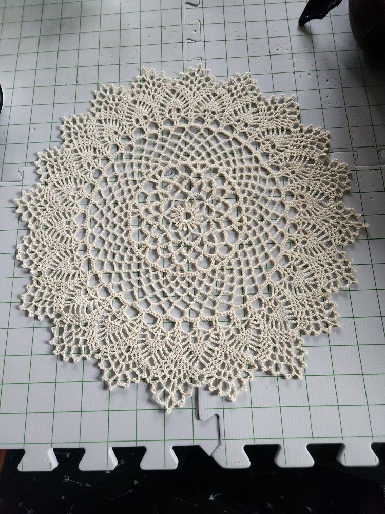Off-white crocheted doily stretched out and pinned on gridded foam tiles for blocking