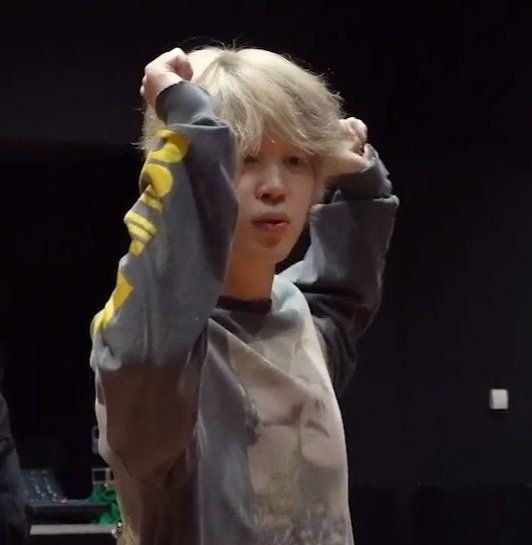 Blonde Jimin wearing a grey long sleeved shirt, arms up during dance practice.