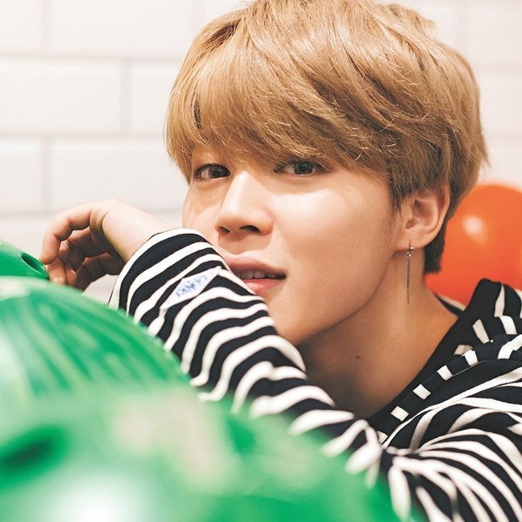 Jimin wearing a striped long sleeved shirt and posing behind a row of bowling balls.