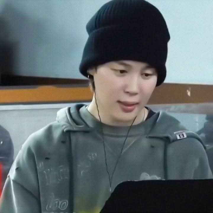 Jimin with a grey long sleeved shirt and a black beanie. He is listening to a song through his earphones.