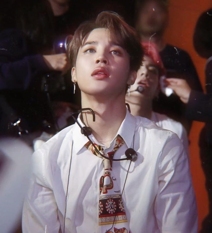 Jimin in a white long sleeved shirt watching a video backstage.