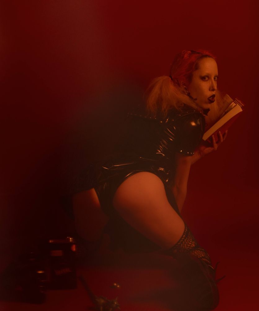 Heidi is down on her knees in a red room and presents you her perfectly tight booty in small shiny pvc panties under a pvc dress. She is looking over her shoulder with a book of spells in her hand. 