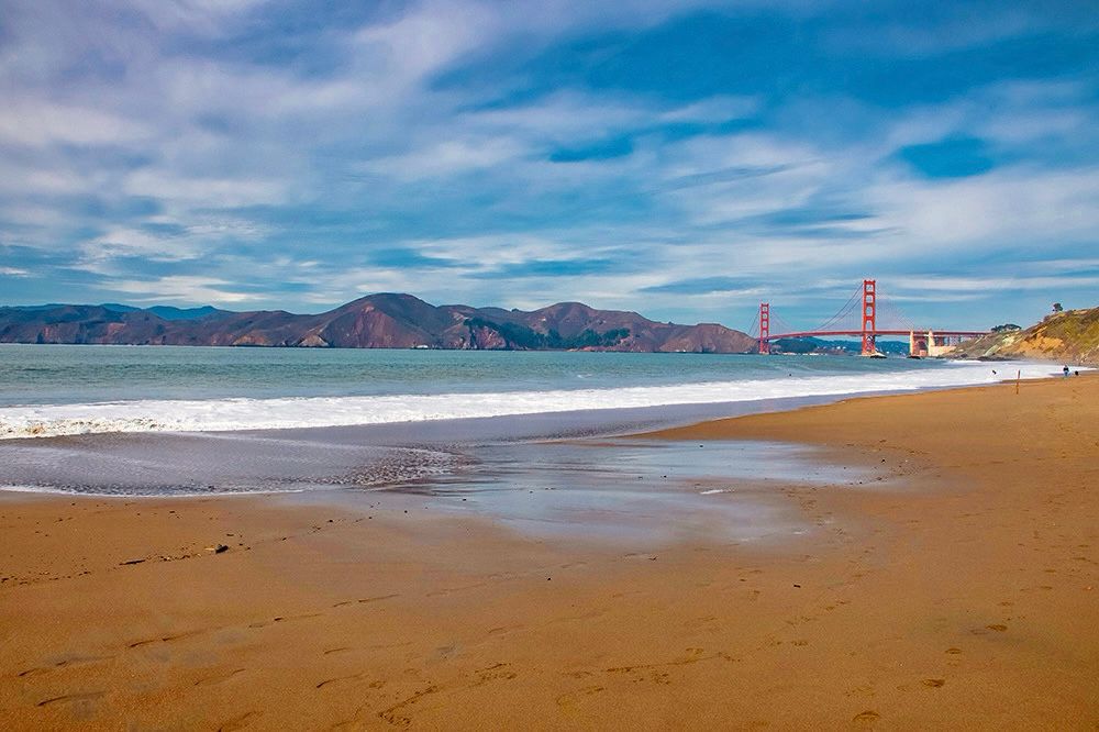 Baker Beach in San Francisco on a partly overcast day. Golden Gate Bridge is seen in the distance to the right, the Marin Headlands to the left 