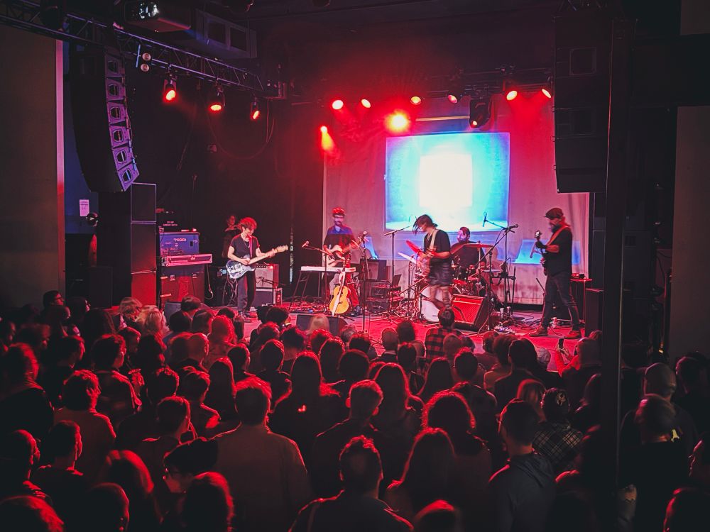 Five-person band fronted by singer, songwriter, and guitar player Ezra Furman, delivering a concert to an attentive audience at a packed nightclub. 