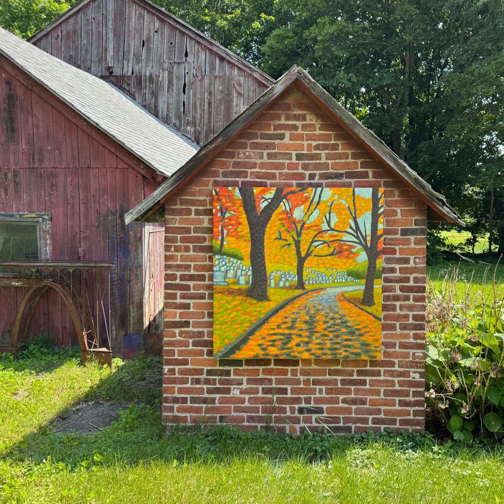 A portal into autumn. Photograph of a series of barn structures. One of them has a painting hung on its side. The painting is of an autumn scene set in a cemetery. 
