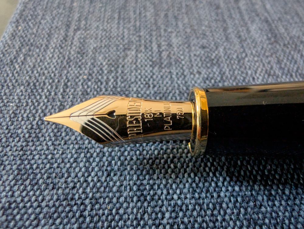 A gold fountain pen nib against a blue fabric backdrop.